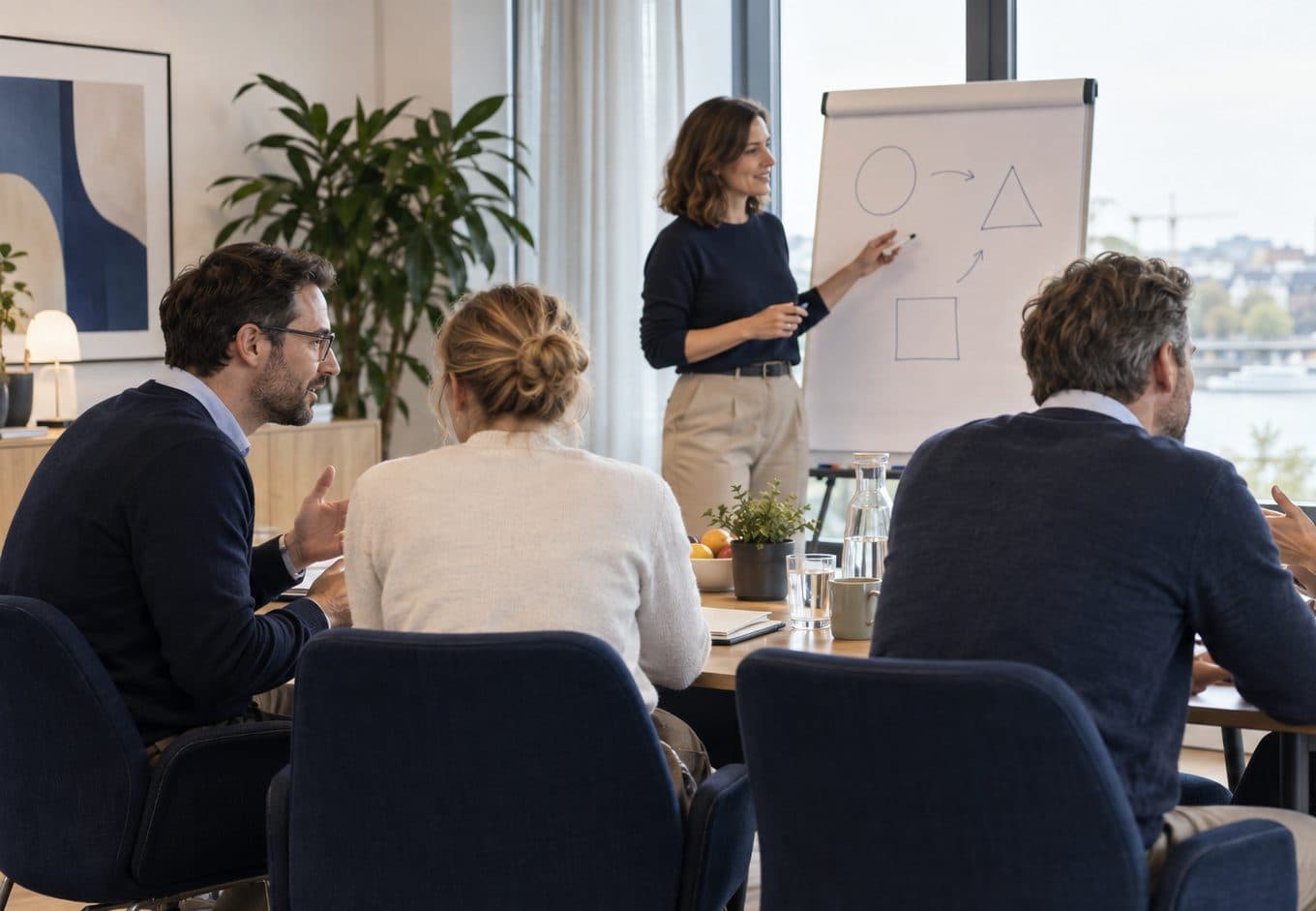 Kleine Runde am Flipchart: eine Referentin erklärt, drei Teilnehmende diskutieren am Tisch.